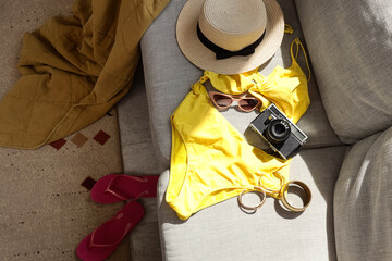 Yellow swimsuit with photo camera and accessories on sofa in living room, top view