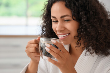 Young African-American woman drinking coffee after shower in kitchen, closeup