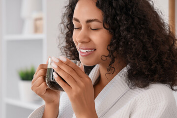Young African-American woman drinking coffee after shower in kitchen, closeup