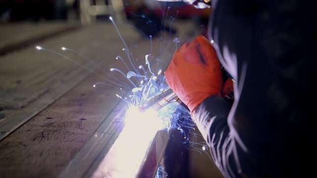 Welder at work, wearing protective gear, welding helmet and heavy-duty cloth. Bright blue and orange sparks are flying as welding torch fuses metal together. Trailer repair