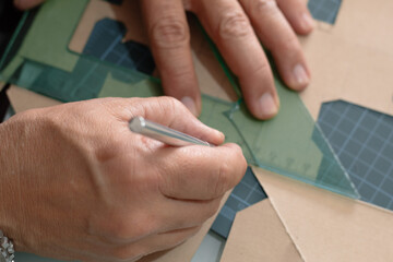 Top view of adult hands cutting cardboard with a utility knife and square on a cutting mat, a safe...