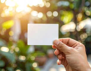Blank business card mockup in hand against bright sunlight and nature bokeh background.