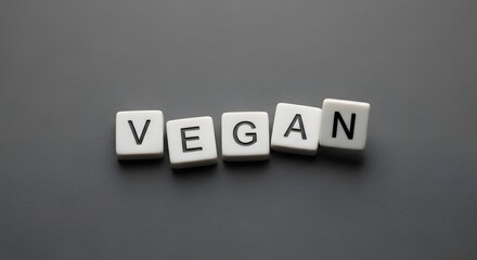 Close-up image of the word "VEGAN" spelled out in white plastic letter tiles on a gray surface.