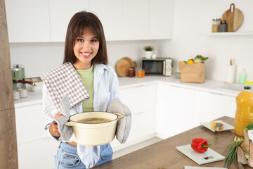 Young woman with tasty soup in kitchen
