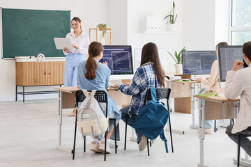 Group of teenage students studying with teacher at school computer lab, back view