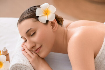 Beautiful young happy woman with white plumeria flower lying on couch in spa salon