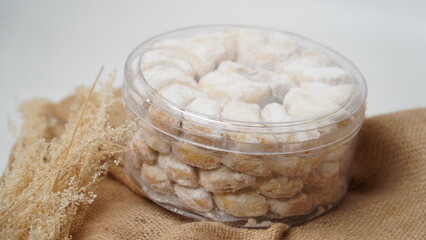 Homemade Putri Salju cookies coated in powdered sugar, stored in a transparent jar. Shot on a clean white background, perfect for festive food promotions and design assets