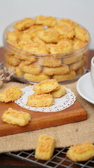 A close-up photo of traditional Indonesian cheese cookies (kastengel) served on a wooden board with a decorative lace paper doily
