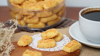A close-up photo of traditional Indonesian cheese cookies (kastengel) served on a wooden board with...