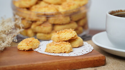 A close-up photo of traditional Indonesian cheese cookies (kastengel) served on a wooden board with a decorative lace paper doily