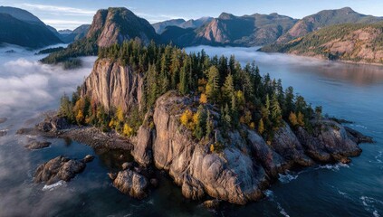 Misty morning aerial view of a rocky island covered in evergreen trees, surrounded by calm water and mountains