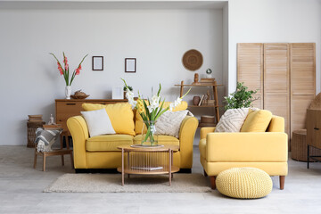 Obraz premium Interior of living room with yellow sofa, armchair and gladiolus flowers in vases