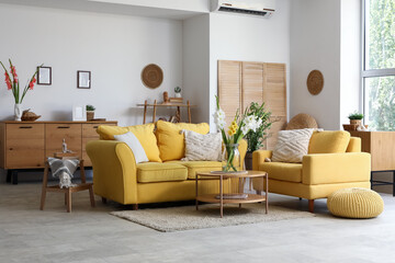 Interior of living room with yellow sofa, armchair and gladiolus flowers in vases