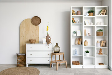 Interior of light room with commode, bookshelf and gladiolus flowers