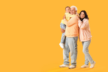 Little girl with her grandparents in hoodies on yellow background
