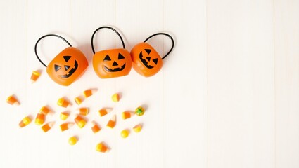 Three jack o lantern candy buckets spill candy corn on a white wooden surface