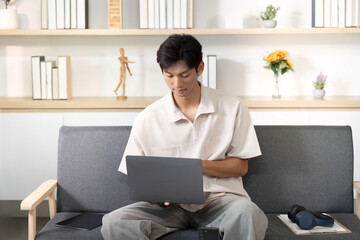 Casual Workspace. Young man using laptop on sofa at home.