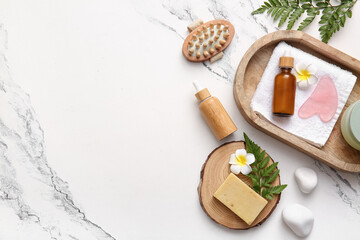 Spa composition with tray, massage body brush and bottles of cosmetic products on marble background