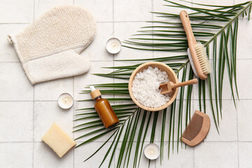 Spa composition with tropical leaf, burning candles and bottle of cosmetic product on white tile background