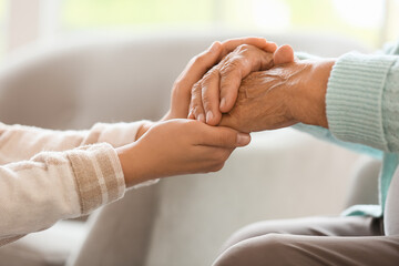 Senior woman with daughter holding hands at home, closeup