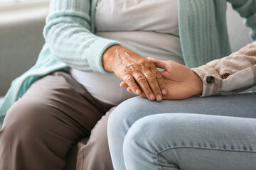 Senior woman with daughter holding hands at home, closeup