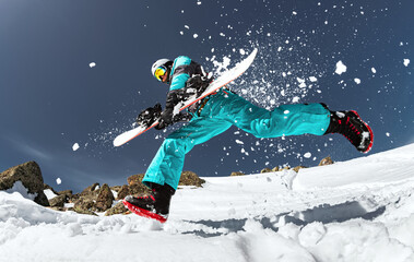 Bottom view of snowboarder jumping in fresh powder snow on winter day in sunny mountains