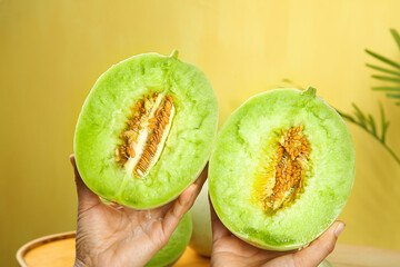 Fresh Jade Green Honeydew Melon Halves with Seeds Held in Hands Against Yellow Tropical Background