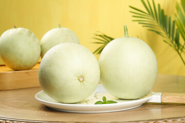 Fresh Jade Melons with Cream Skin on White Plate with Palm Leaves Background