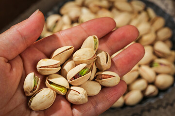 Hand holding roasted pistachios with open shells and green nuts in palm