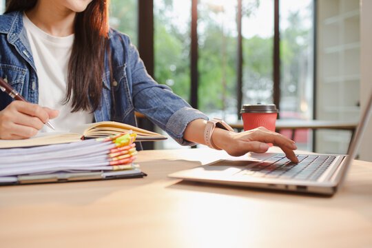 Smiling young Asian woman clearing paperwork in office, using laptop and many documents beside her. Accounting and finance business concept. - Powered by Adobe