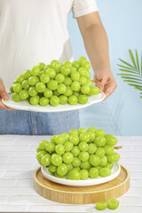 Fresh Green Seedless Grapes on White Plates in Sunny Kitchen Setting with Person Serving Healthy Fruit