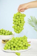 Fresh Green Grapes Bunch Held by Hand on Bright White Background with Palm Leaf Decoration