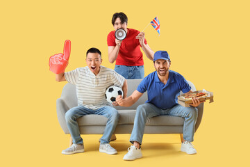 Male sports fans with UK flag watching football on sofa against yellow background