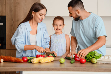 Happy parents with their little daughter cutting cucumber in kitchen