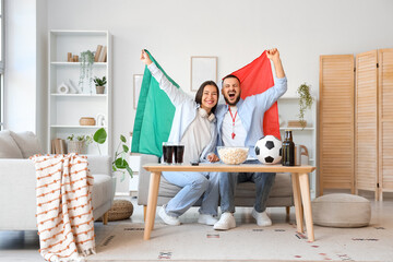 Young couple with Mexican flag watching football at home