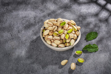 Fresh Pistachio Nuts in Bowl with Green Leaves on Gray Background