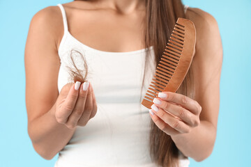 Young woman with comb and hair loss problem on blue background, closeup