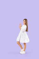 Teenage girl in white dress pointing at something on lilac background