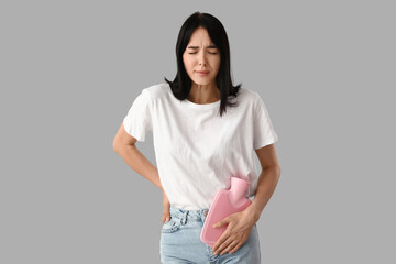 Young woman with hot water bottle suffering from menstrual cramps on light background