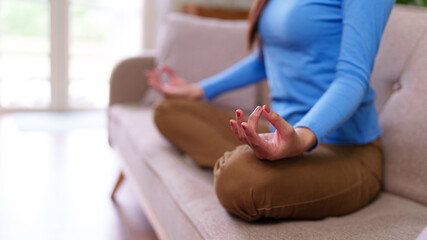 Asian adult woman meditating on sofa at home finding peace calm relaxation mindfulness practicing yoga indoors self care wellness spiritual journey
