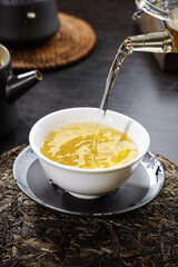 Traditional Tea Ceremony - Hot Golden Tea Pouring from Glass Teapot into White Cup with Loose Tea Leaves