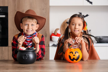 Little children dressed for Halloween with candies at table in kitchen