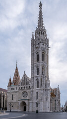 Fototapeta premium Budapest, Hungary – Architectural detail of Matthias Church in the Castle District, showcasing Neo-Gothic spires, diamond-pattern roof tiles, sculpted façades, and ornate stone carvings.
