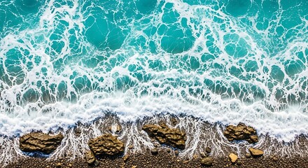 Aerial view of turquoise ocean waves crashing against rocky shoreline with pebbles creating a dynamic and natural scene of coastal beauty