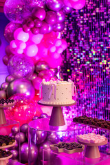 Elegant birthday party table with cake, chocolates, and pink metallic balloon decoration with glitter backdrop