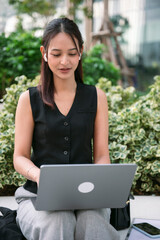 Businesswoman working remotely with laptop and earbuds outdoors