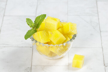 Fresh Yellow Watermelon Cubes in Glass Bowl with Mint Garnish on White Wood Background