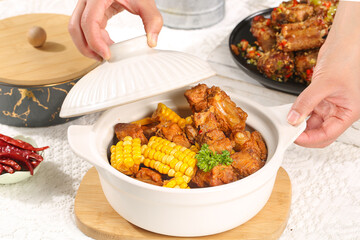 Fresh boiled pork ribs and corn dish with hands reaching for homemade meal on wooden serving board