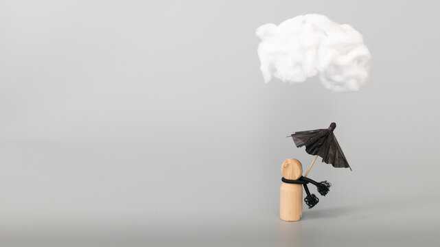 Psychology, solitude, fear or mental health problem concept. Depressed sad person with a cloud overhead, on grey background. Wooden figure with black umbrella symbolize mental health. 
