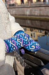 Handmade knitted gloves on female hands. Woman wearing blue patterned mittens outdoor. Warm outfit for winter and autumn. Craft street style